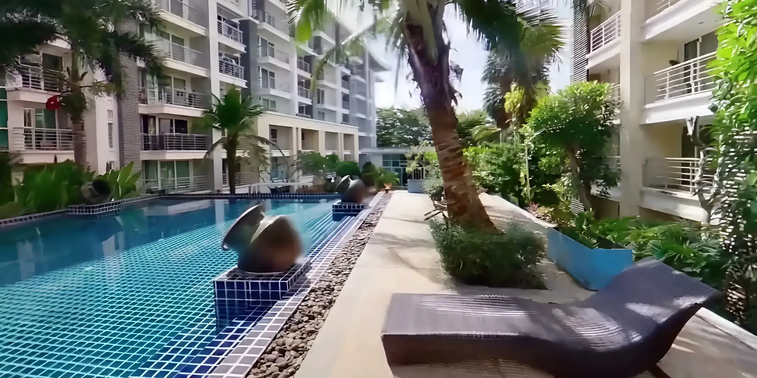 Large tropical swimming pool lined with palm trees at The Royal Place Condominium Phuket